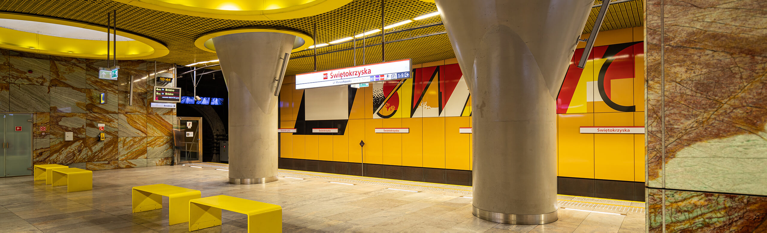 Waiting area with yellow walls and benches in a metro station in Warsaw.